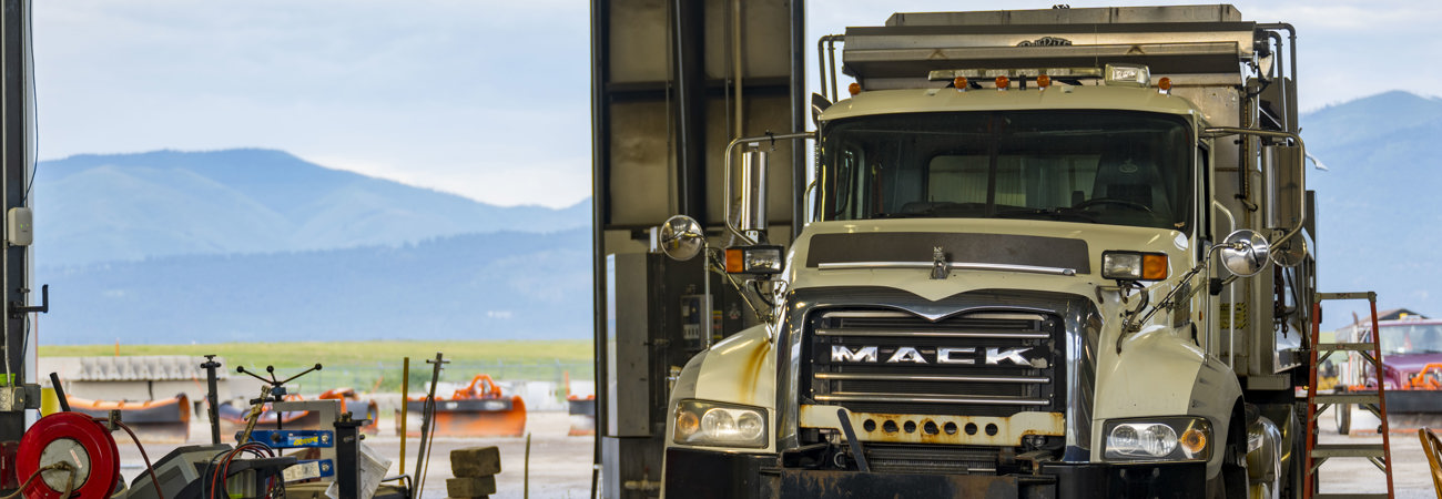 A Mack truck in the Public Works shop, with mountains visible in the background