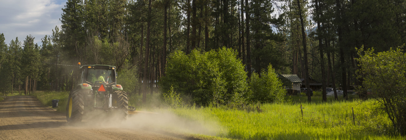 Tractor on a gravel road with trees in the background, dust is visible