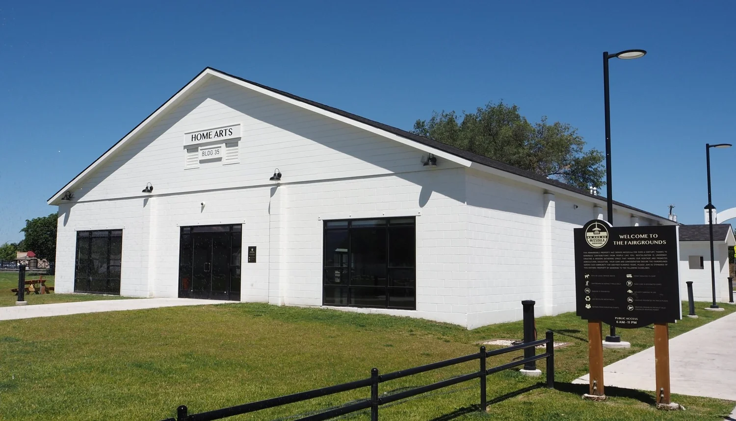 White Fairgrounds Home Arts Building Surrounded By Blue Sky And Green Grass